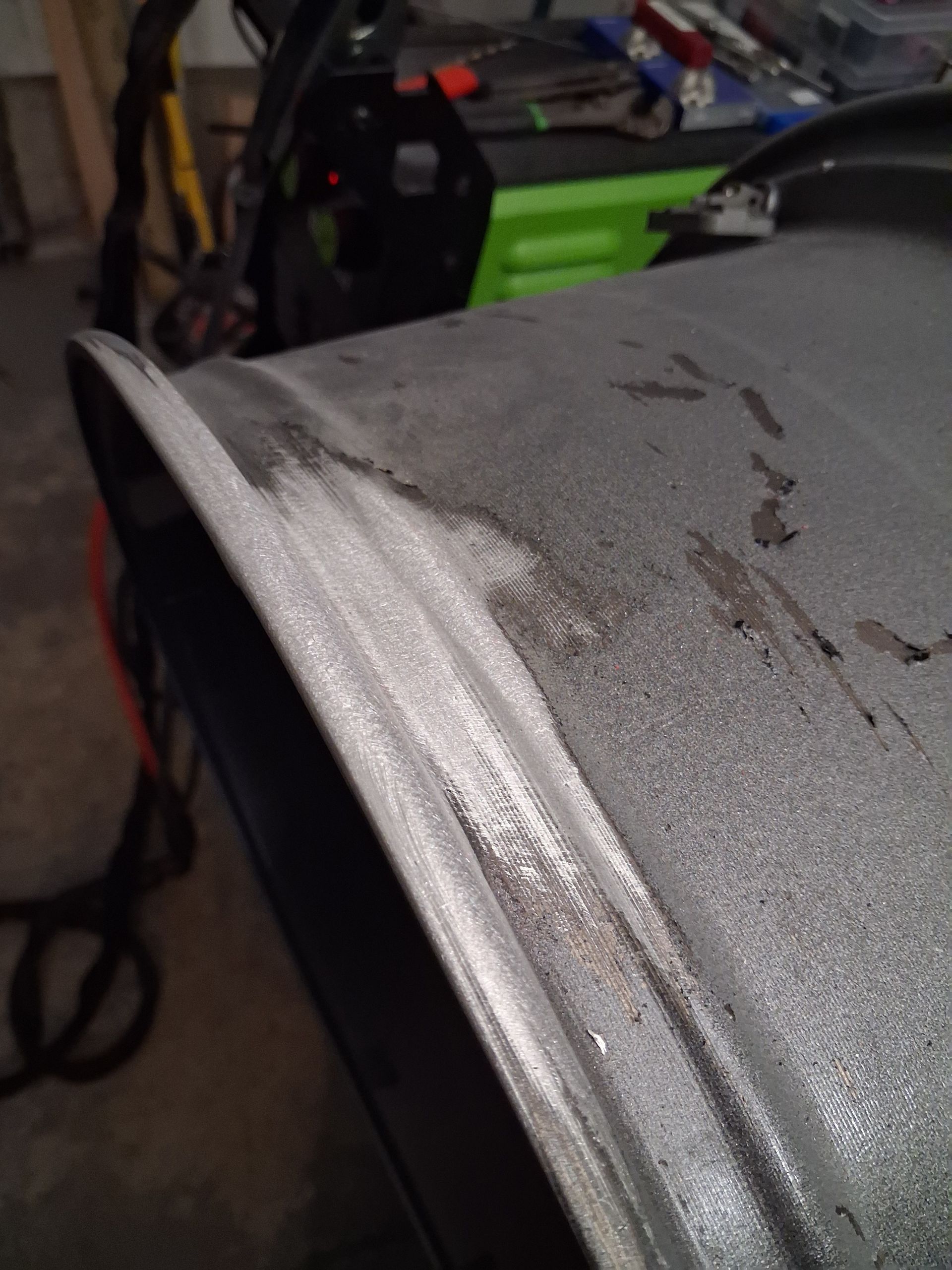 Close-up of a scratched gray metal surface with a bright silver edge in a workshop area