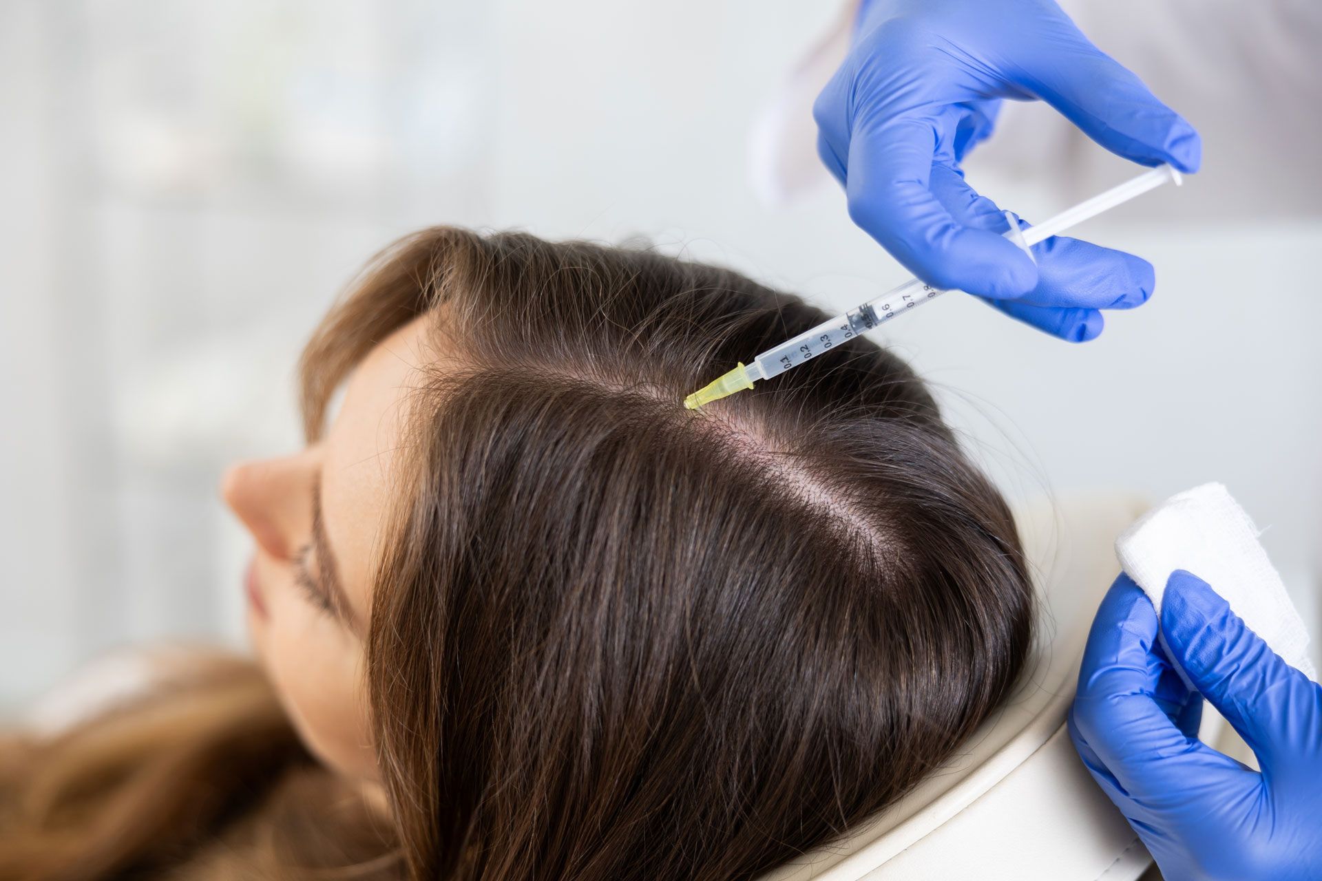 Person receiving scalp injections from a gloved hand.