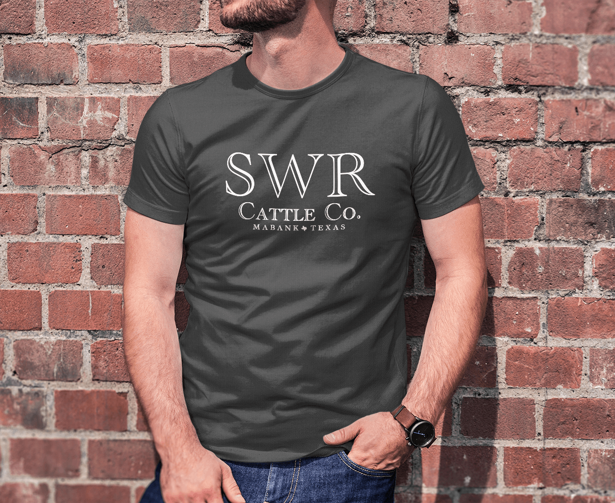 A man wearing a swr cattle co. t-shirt is standing in front of a brick wall