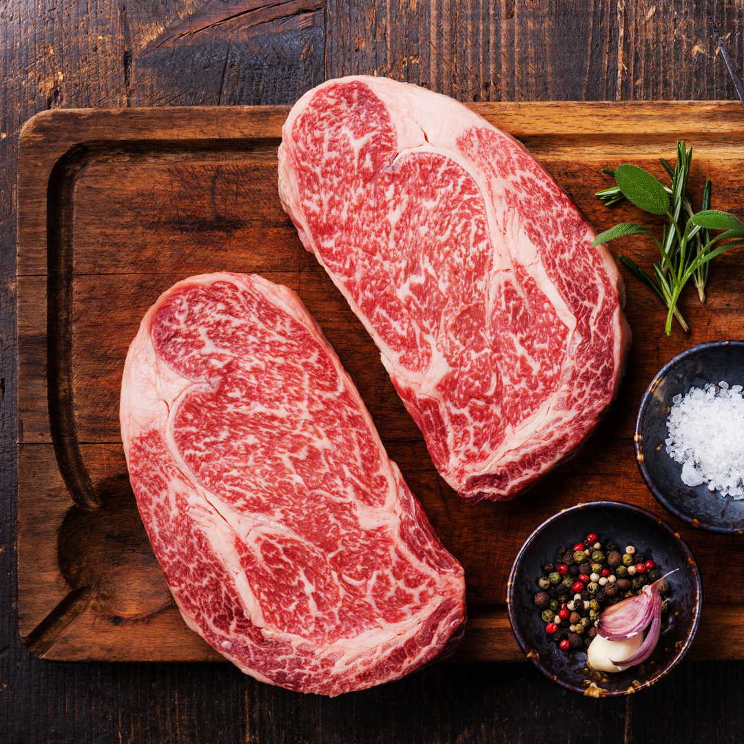 Two raw steaks are sitting on a wooden cutting board.