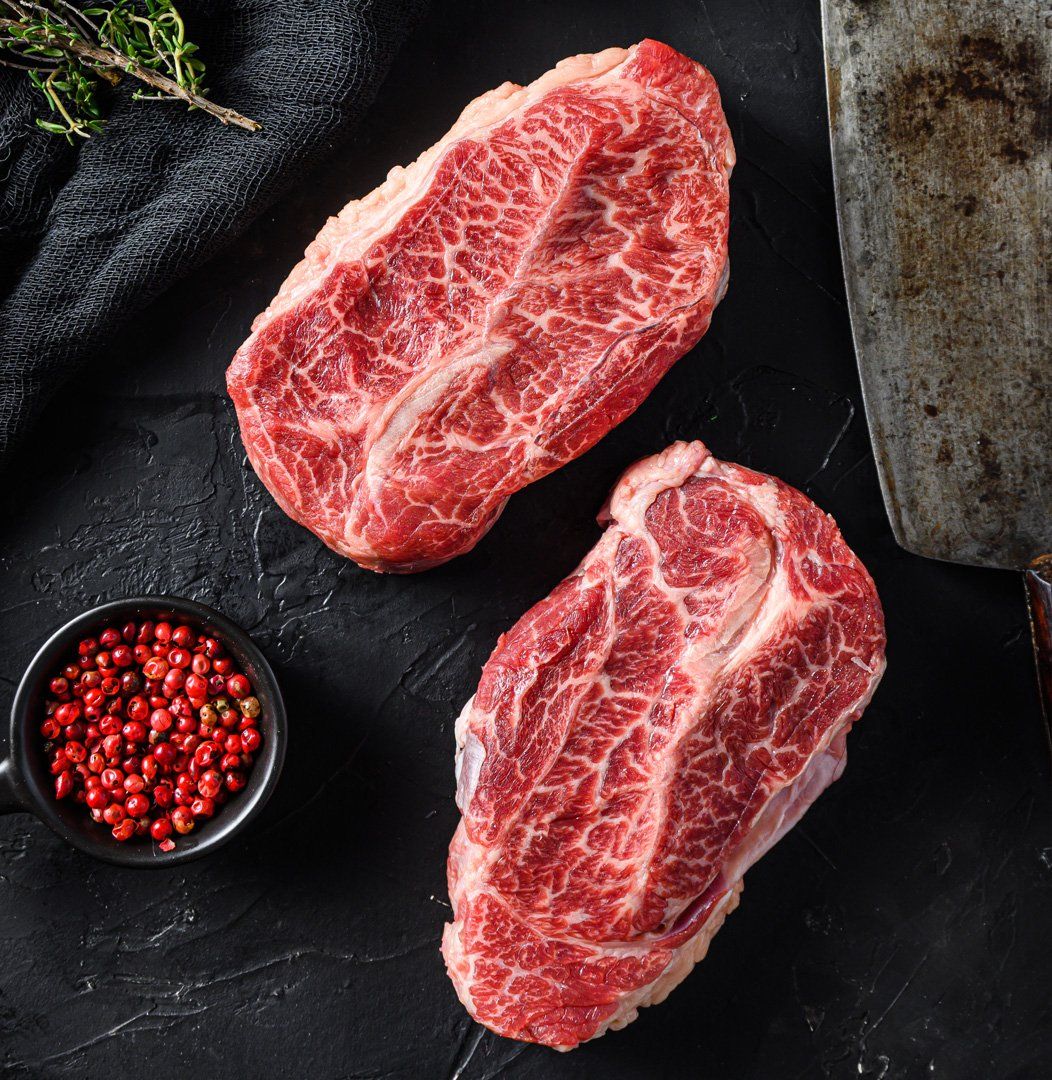 Two raw steaks are sitting on a black table next to a bowl of red pepper.