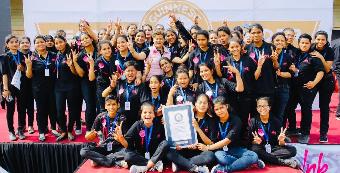 A large group of people in black shirts celebrating on stage, holding a Guinness World Record certificate.
