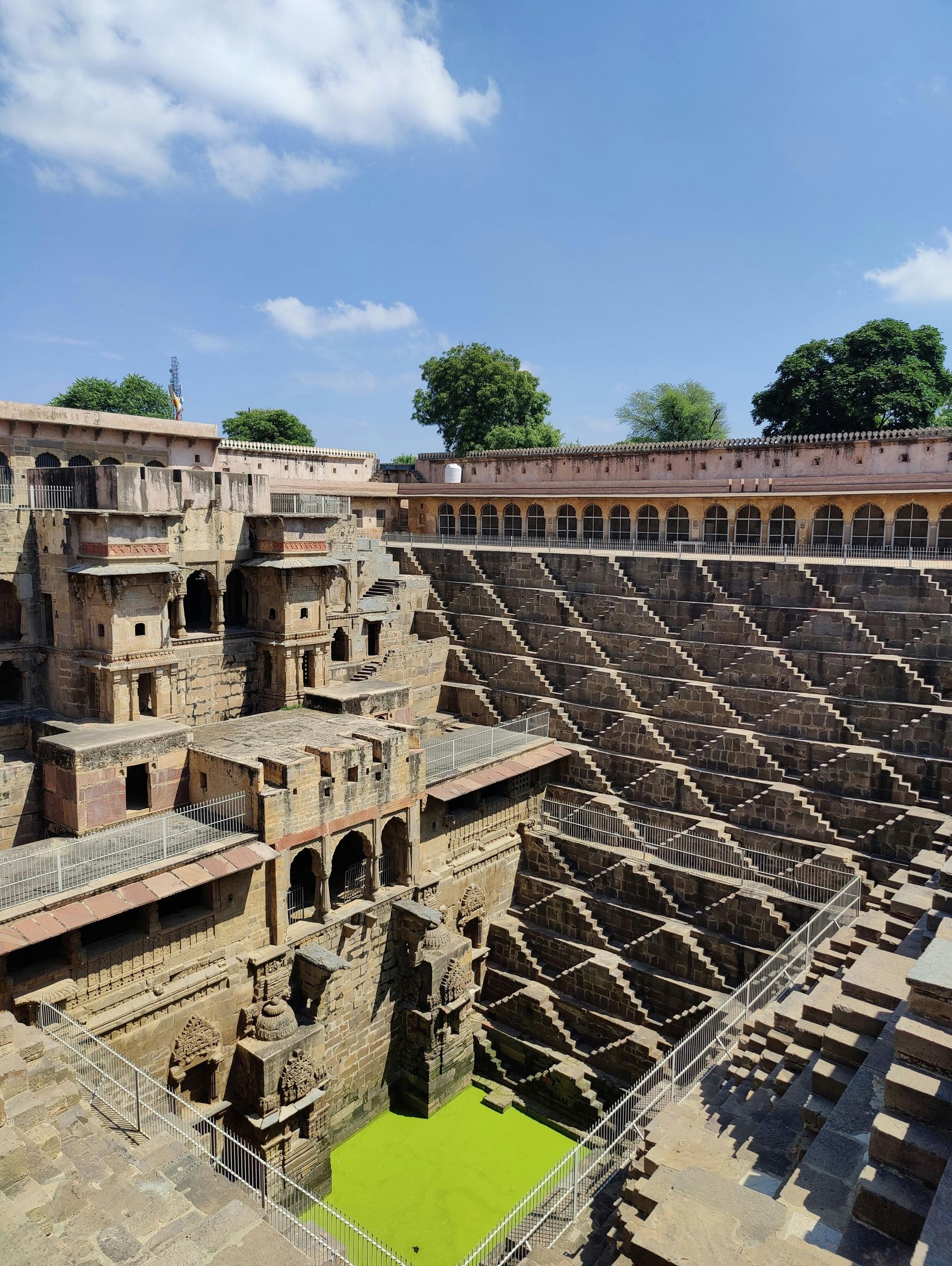 Chand Baori stepwell in Rajasthan, India, featuring intricate stone staircases leading down to a green pool of water.
