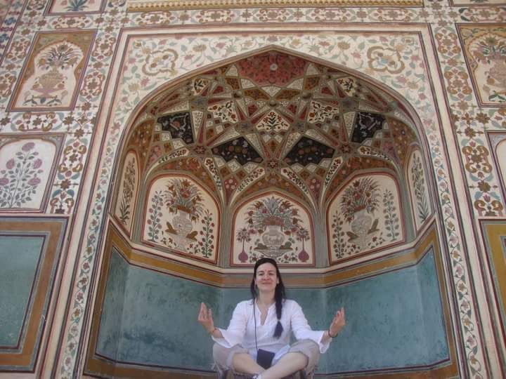 A person sitting in a lotus position, meditating in front of an ornate, patterned wall alcove with floral designs.