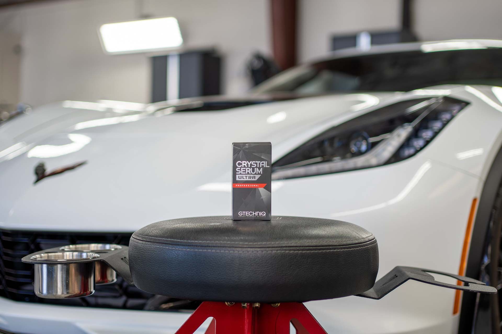 White sports car in a garage, with a tire on a red stand in the foreground