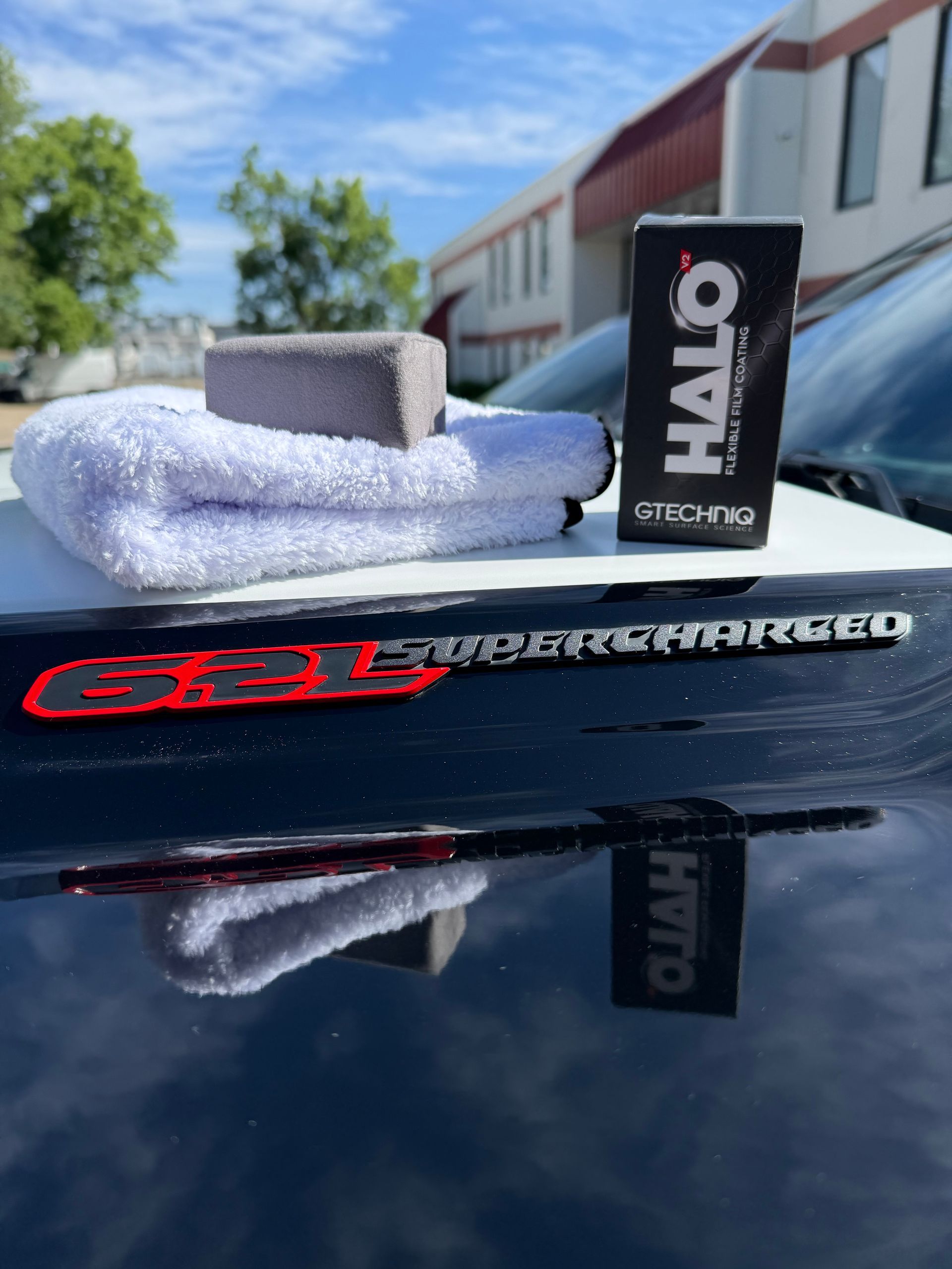 HALO logo on a car hood with a folded white towel and a gray sponge outdoors in sunlight