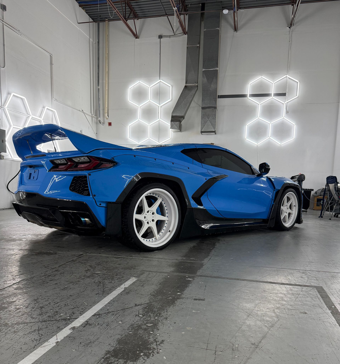 Blue sports car in a garage with bright hexagonal lights on the wall and a wet concrete floor