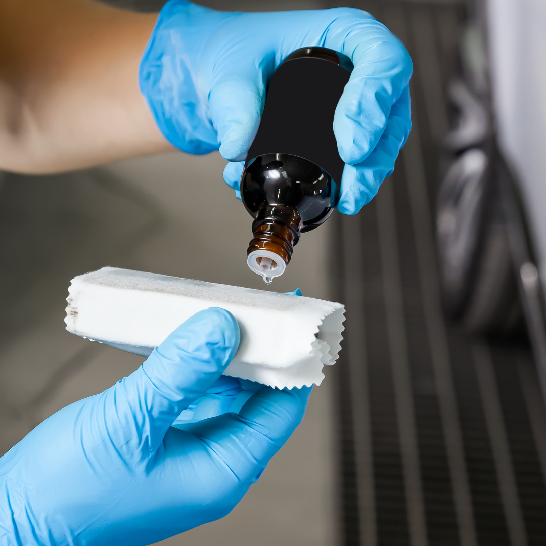 Gloved hands pouring liquid from a bottle onto a white cloth or pad