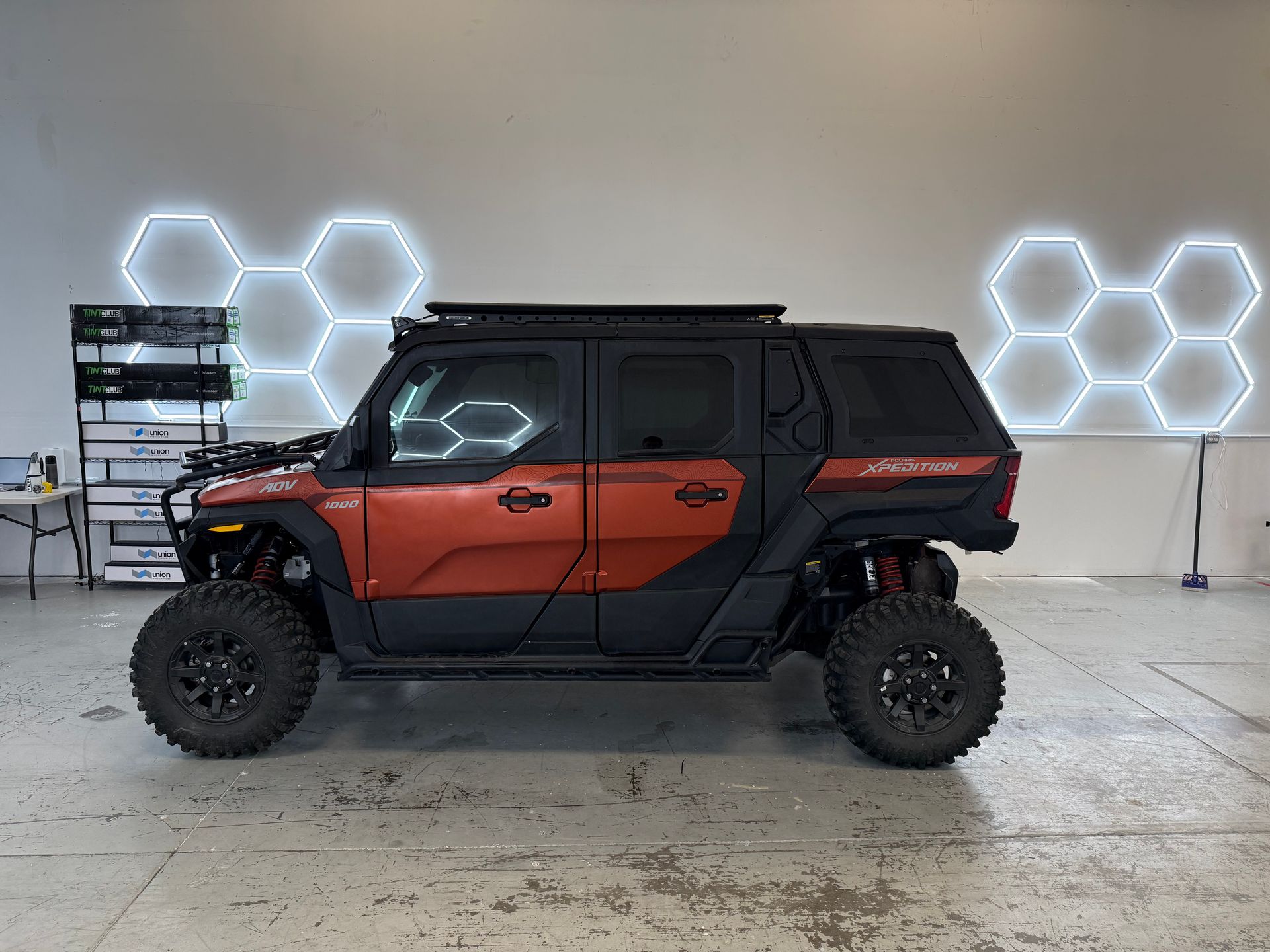 Orange-and-black off-road SUV parked indoors with glowing hexagon wall lights behind it