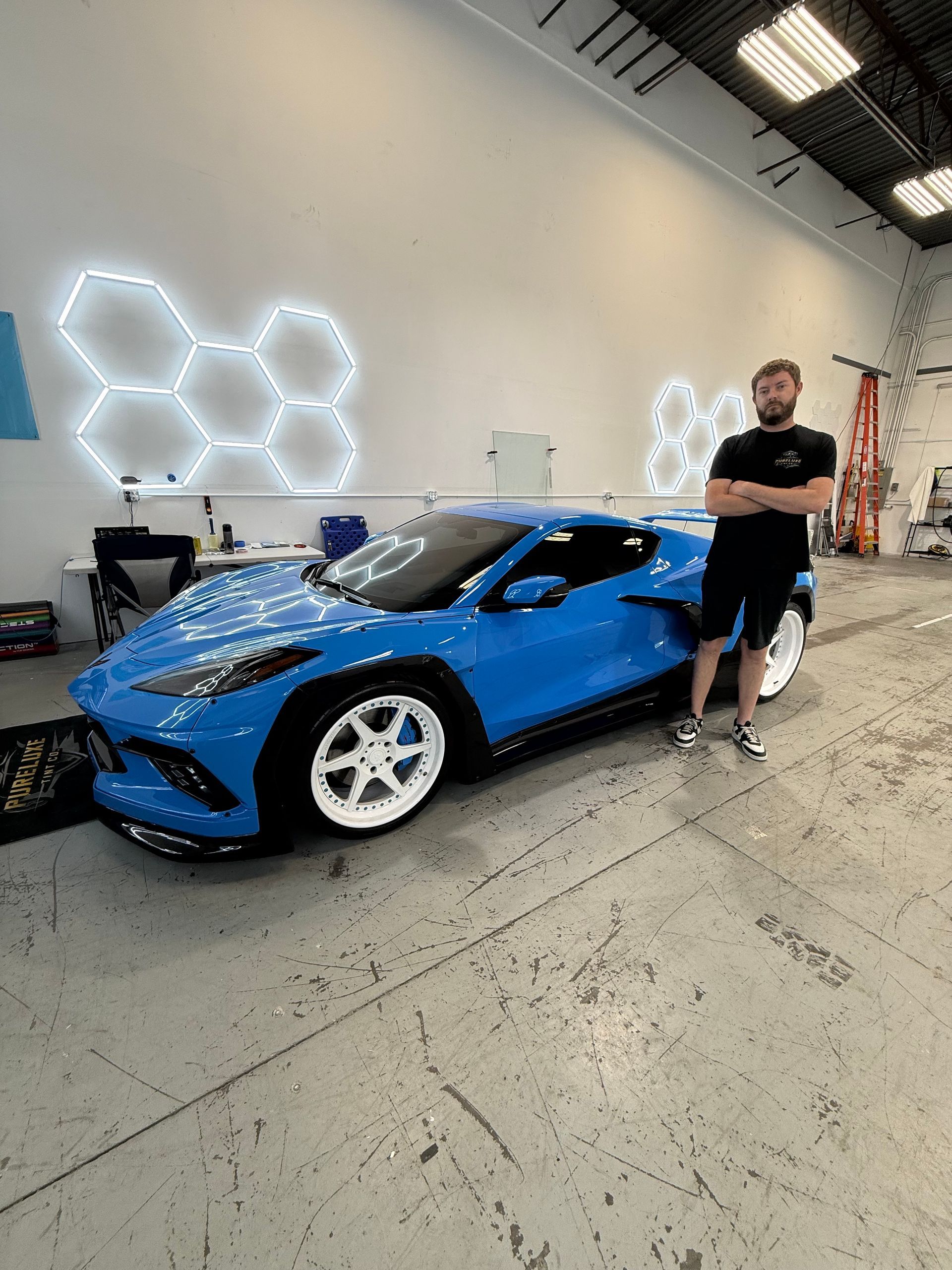 Man standing beside a blue sports car in a bright showroom with hexagonal wall lights