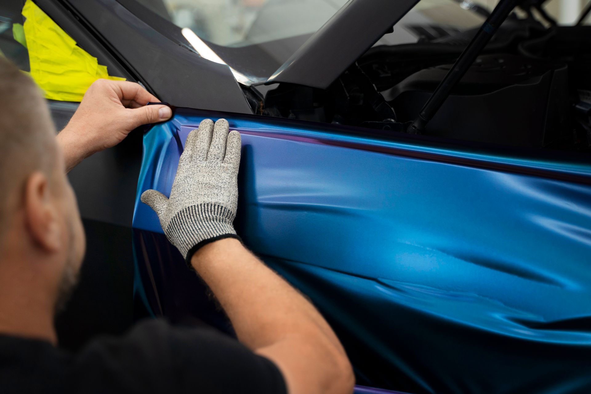 Person applying blue vinyl wrap to a car door with gloved hands