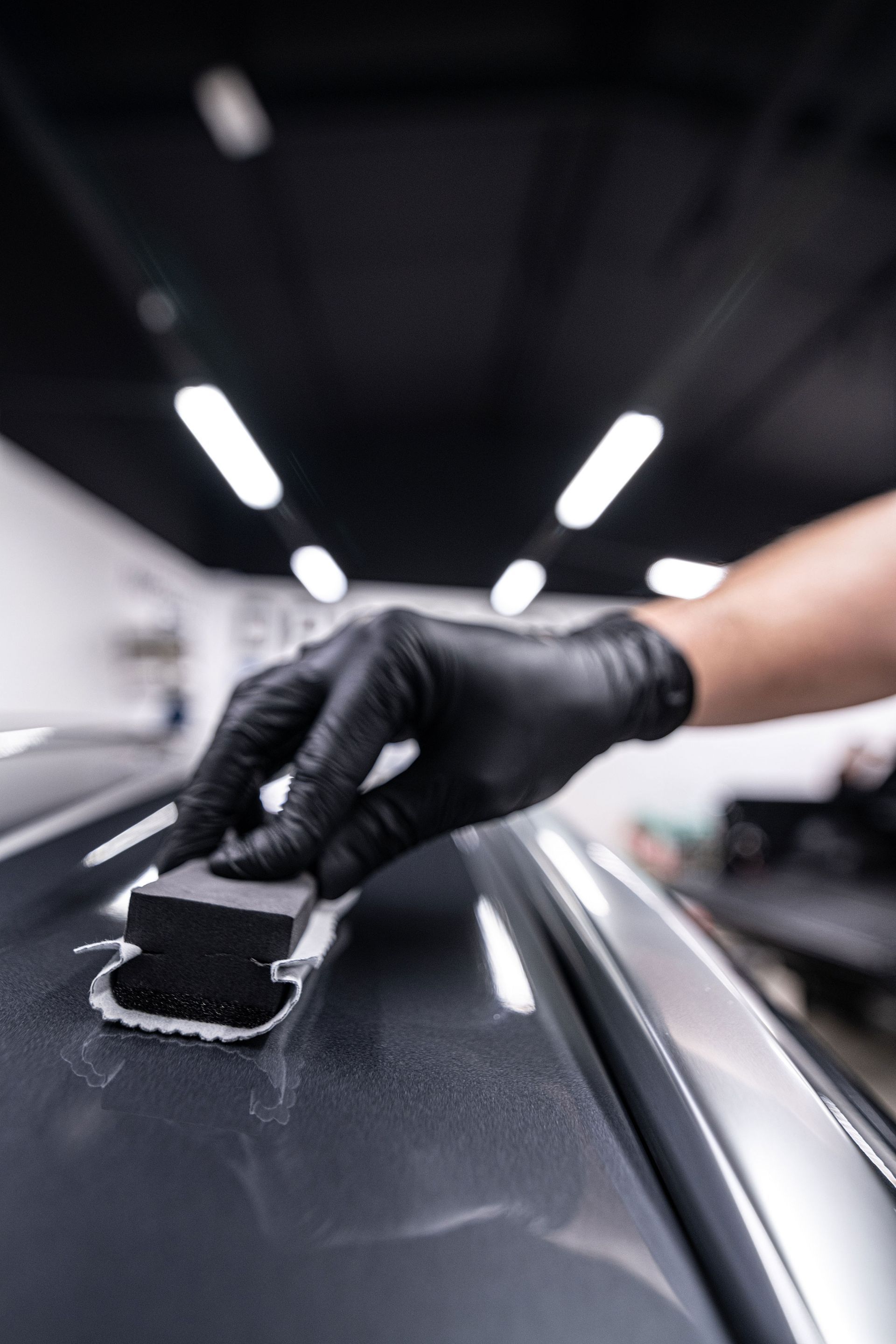 Gloved hand applying polish to a car’s glossy black roof in a garage