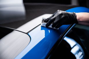 Gloved hand polishing a glossy blue car panel in a detailing shop