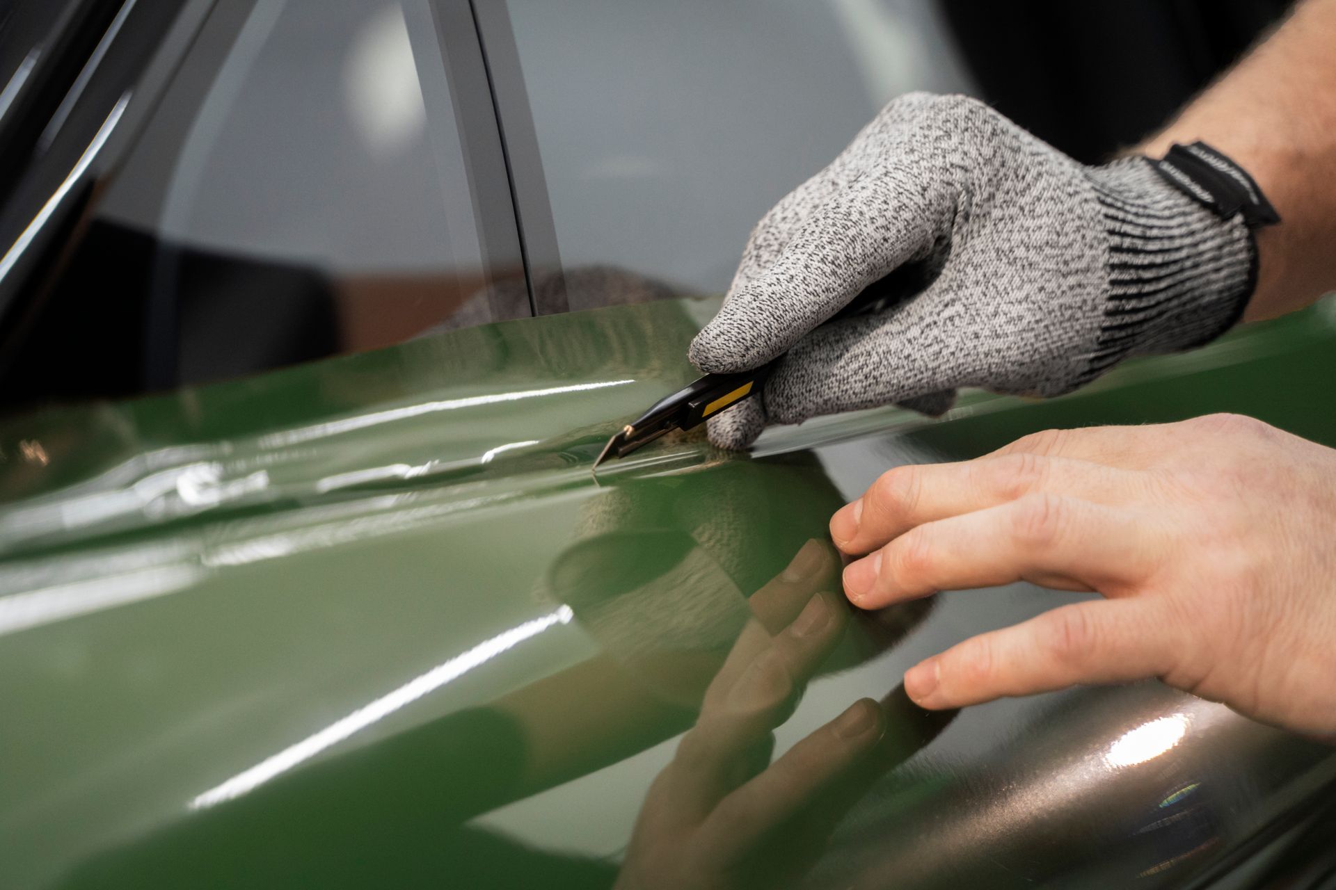 Gloved hands using a squeegee on a green car hood during detailing