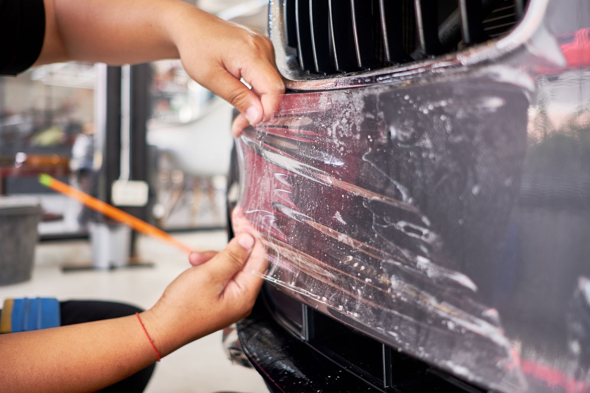 Hands applying clear protective film to the front bumper of a black car