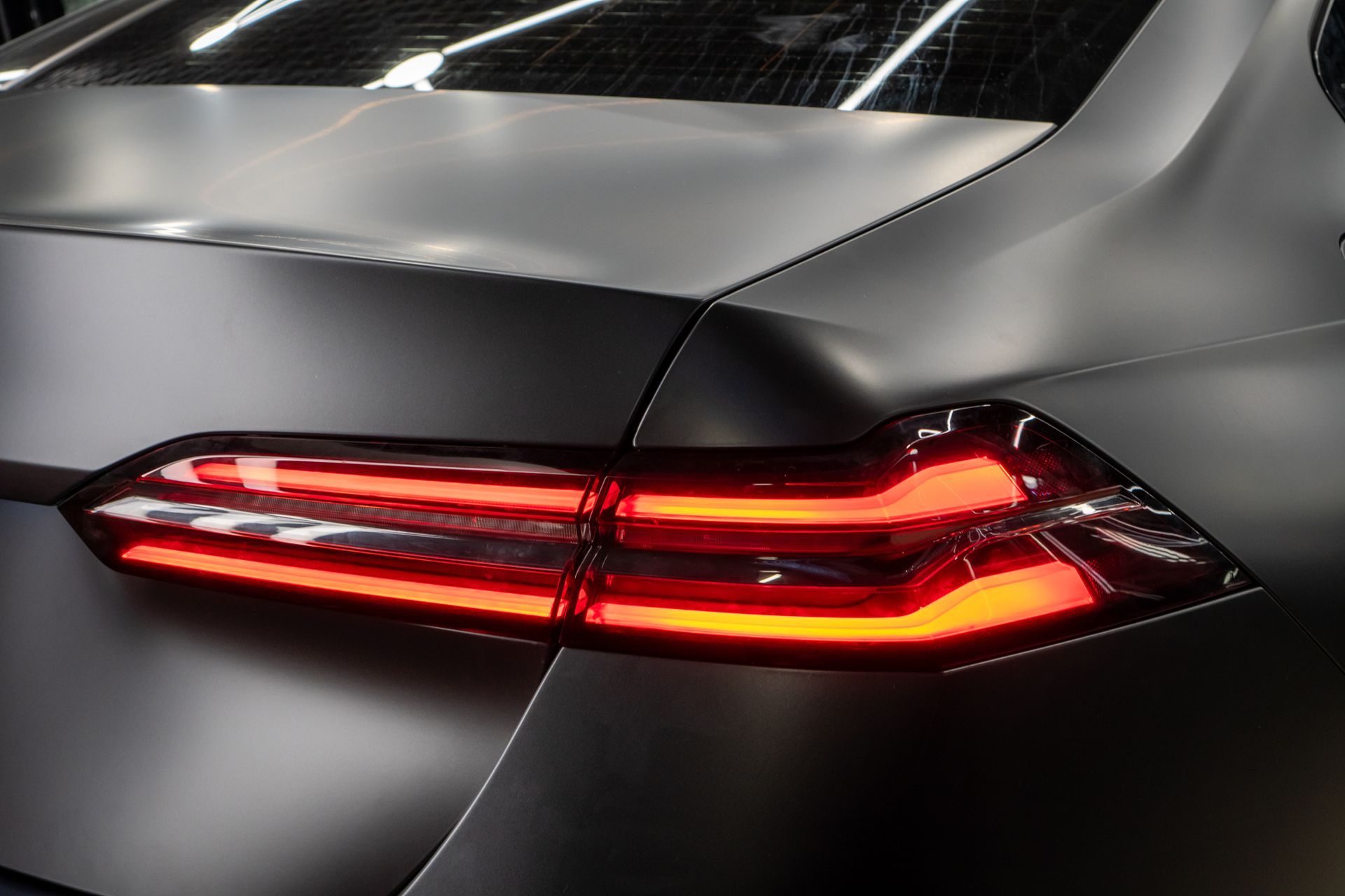Close-up of a car’s rear with illuminated red taillight on a matte black body