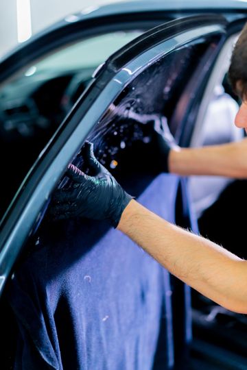 Gloved hands washing a car window with soap suds inside a garage