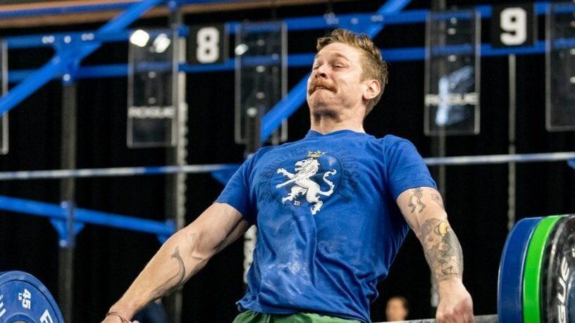 A man in a blue shirt is lifting a barbell in a gym.