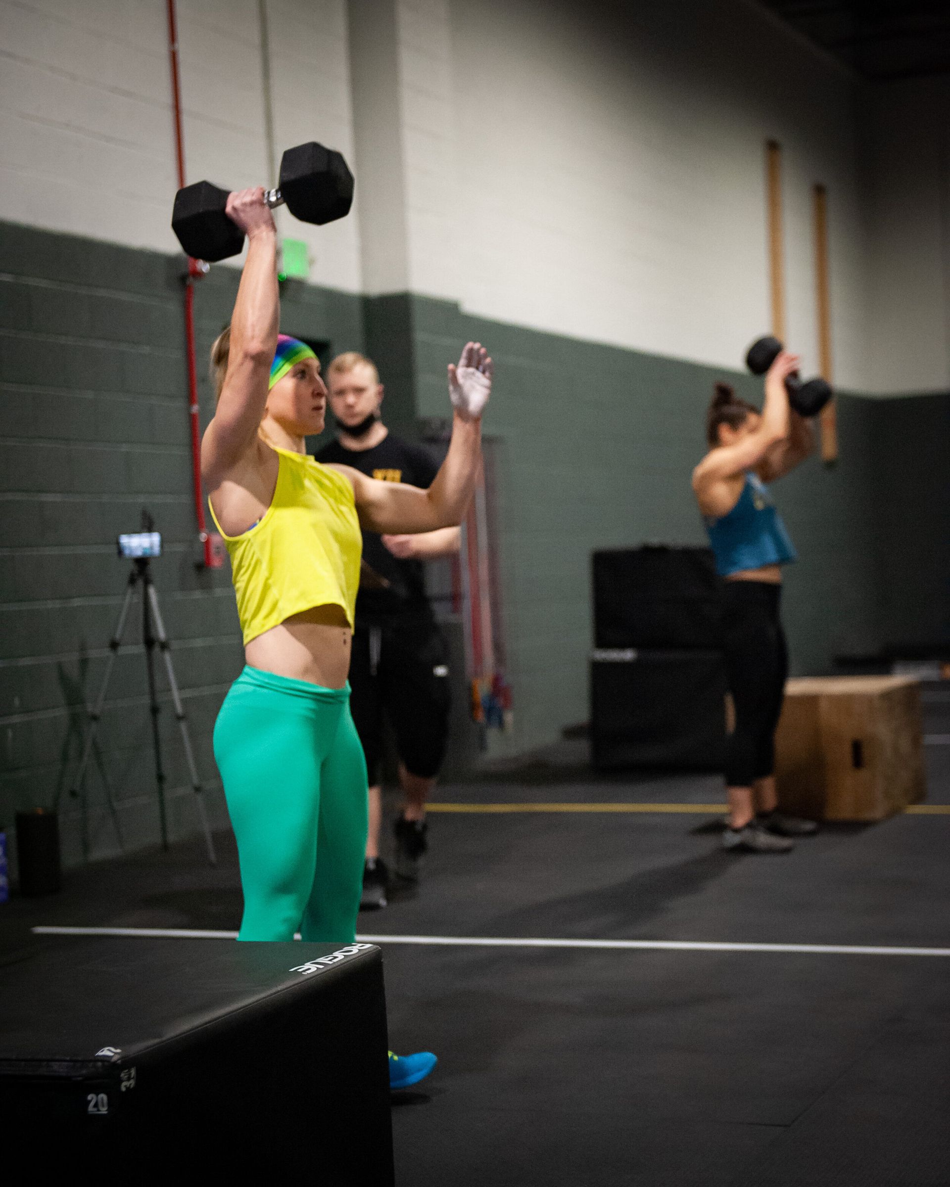 A woman in a yellow shirt is lifting dumbbells in a gym