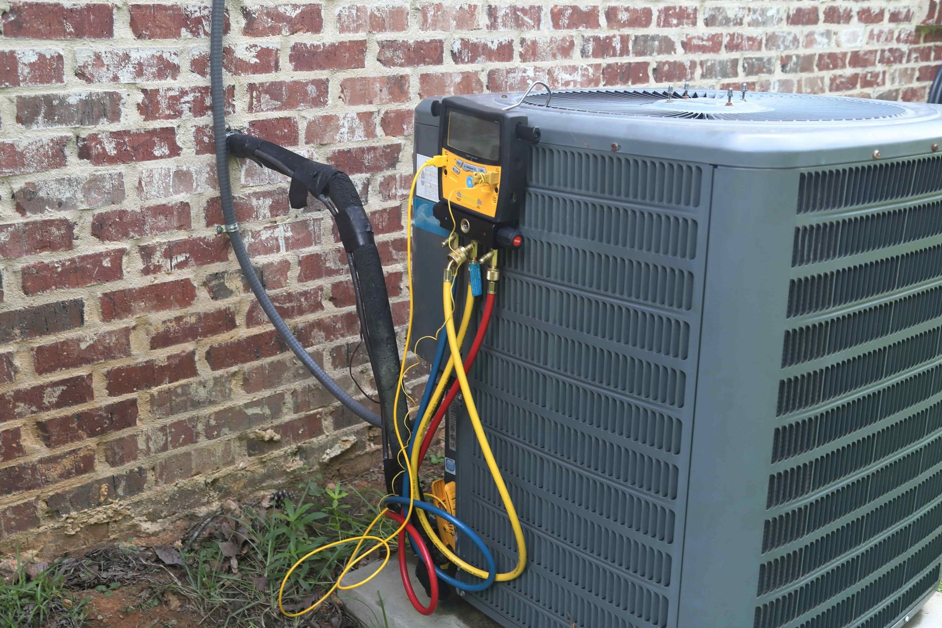 An air conditioner is being serviced by a brick wall.