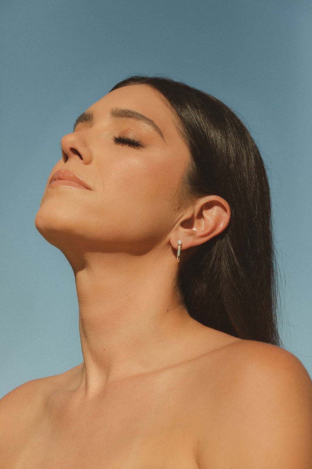 A woman without a shirt is wearing earrings and looking up at the sky.