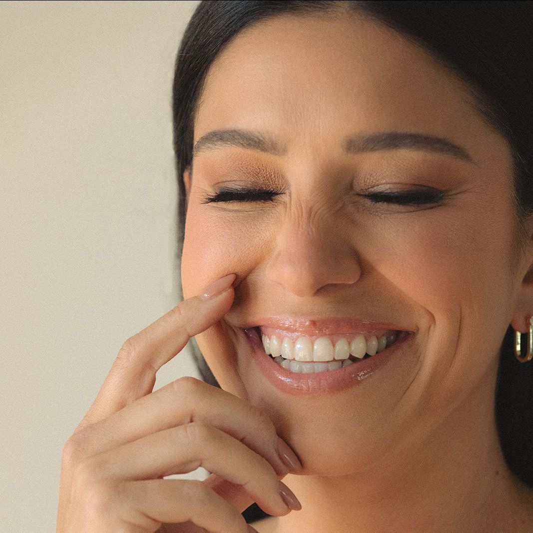 A woman is smiling and touching her face with her finger.