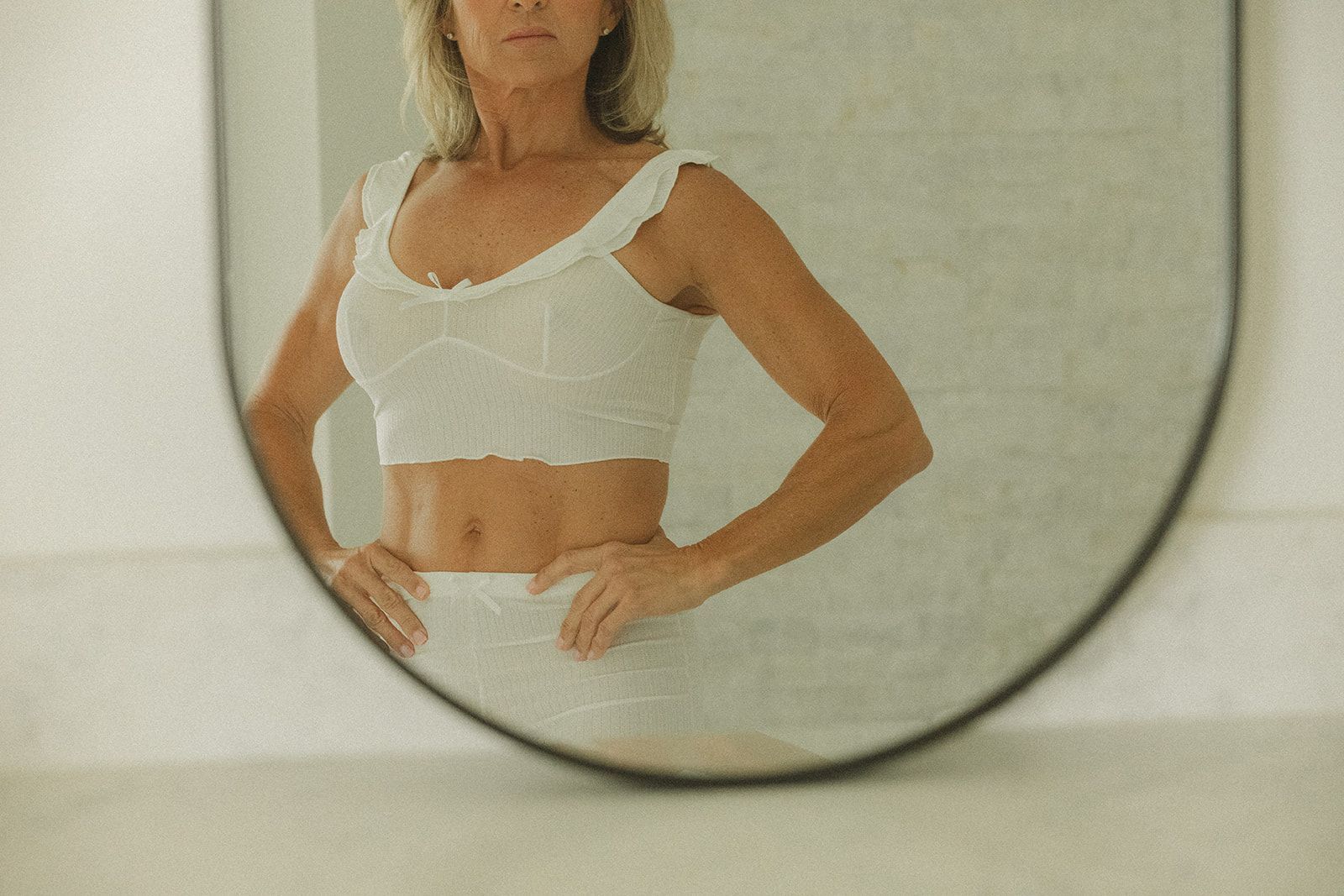 A woman is standing in front of a round mirror.