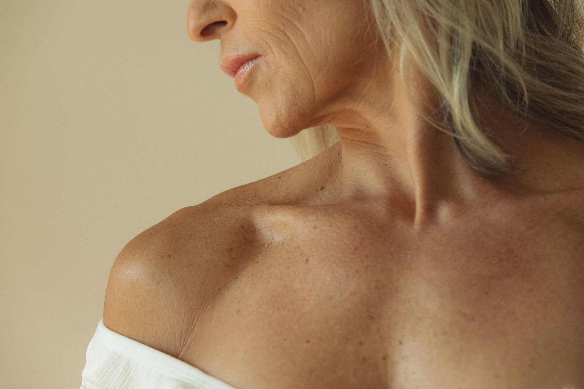 Close-up of an older woman's shoulder and upper chest, showing skin texture and collarbone detail. The woman's profile is visible.