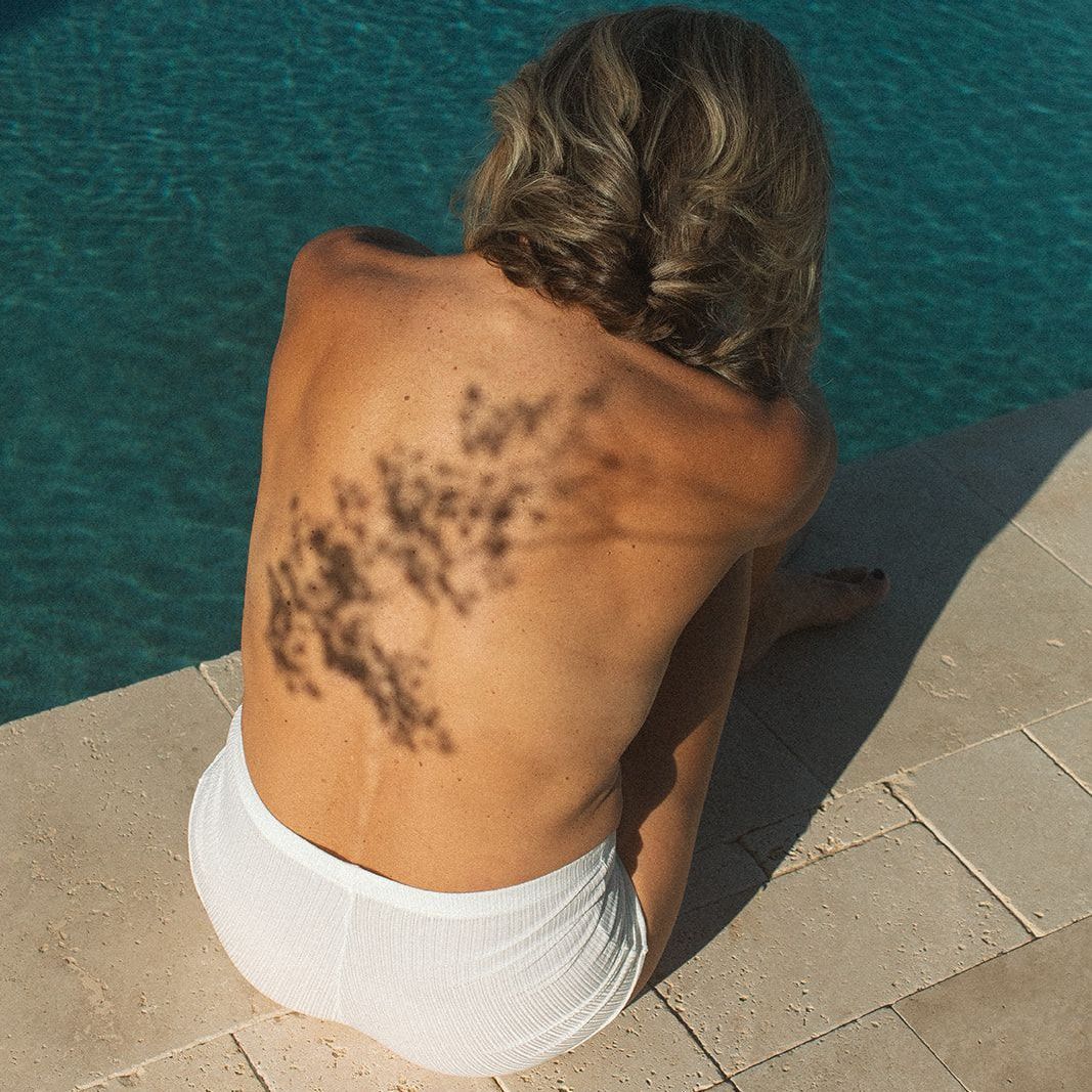 A woman with a tattoo on her back is sitting next to a pool.