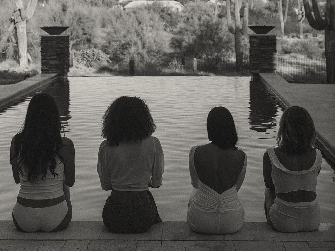 Four women are sitting on the edge of a swimming pool.