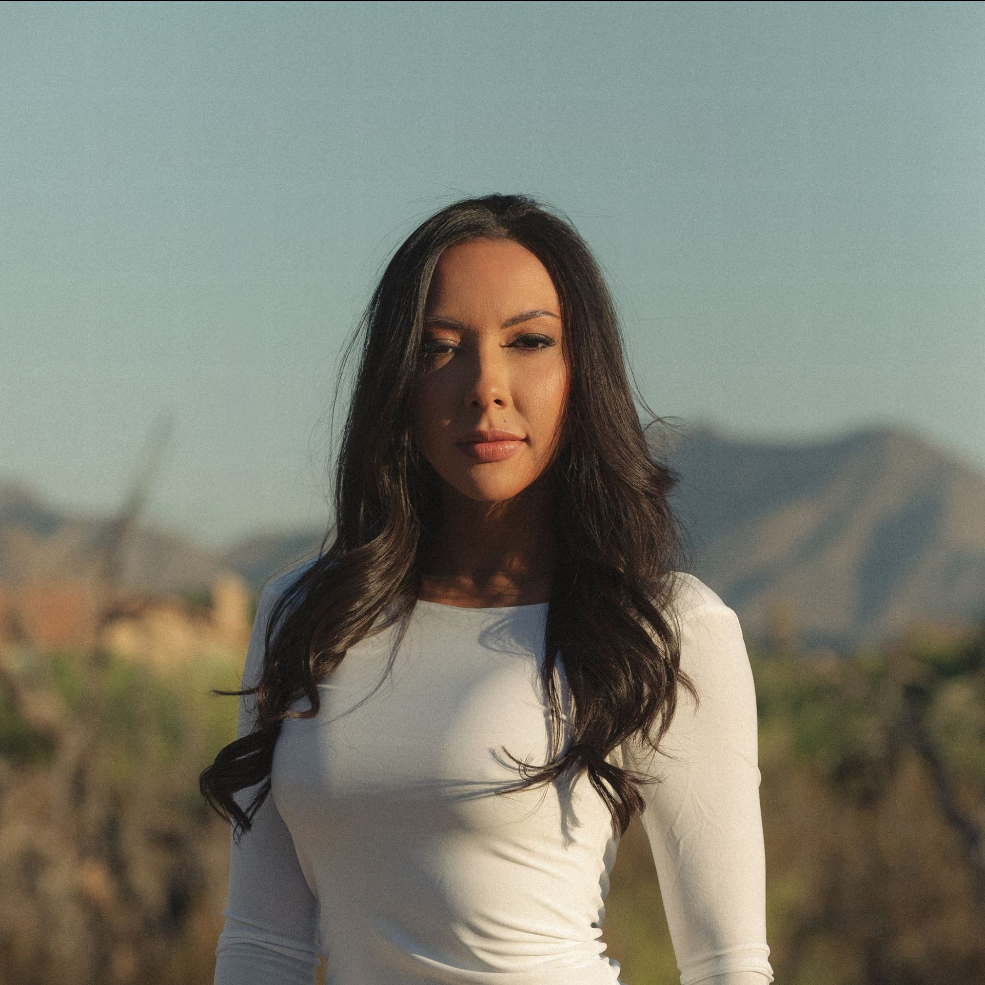 A woman in a white shirt is standing in front of mountains