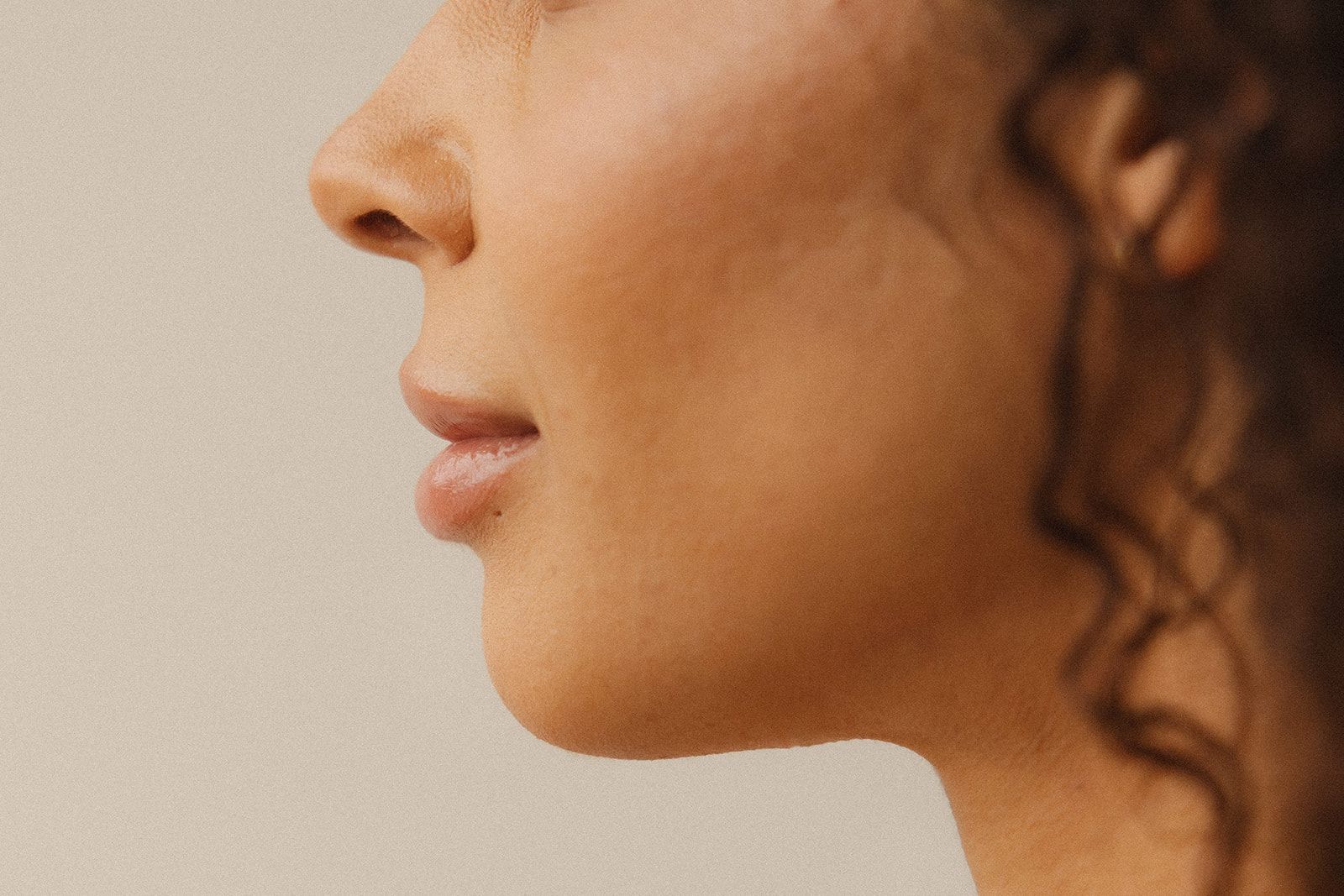 Profile view of a person's jawline and lower face against a soft, neutral-toned background.