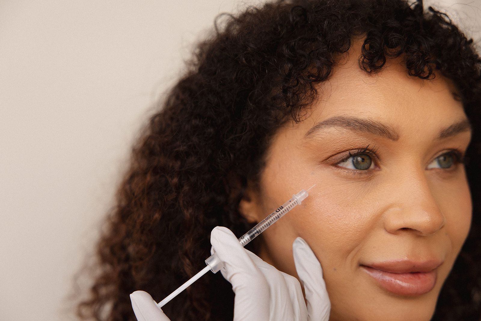 Gloved hand injecting a woman’s cheek with a syringe during a cosmetic procedure