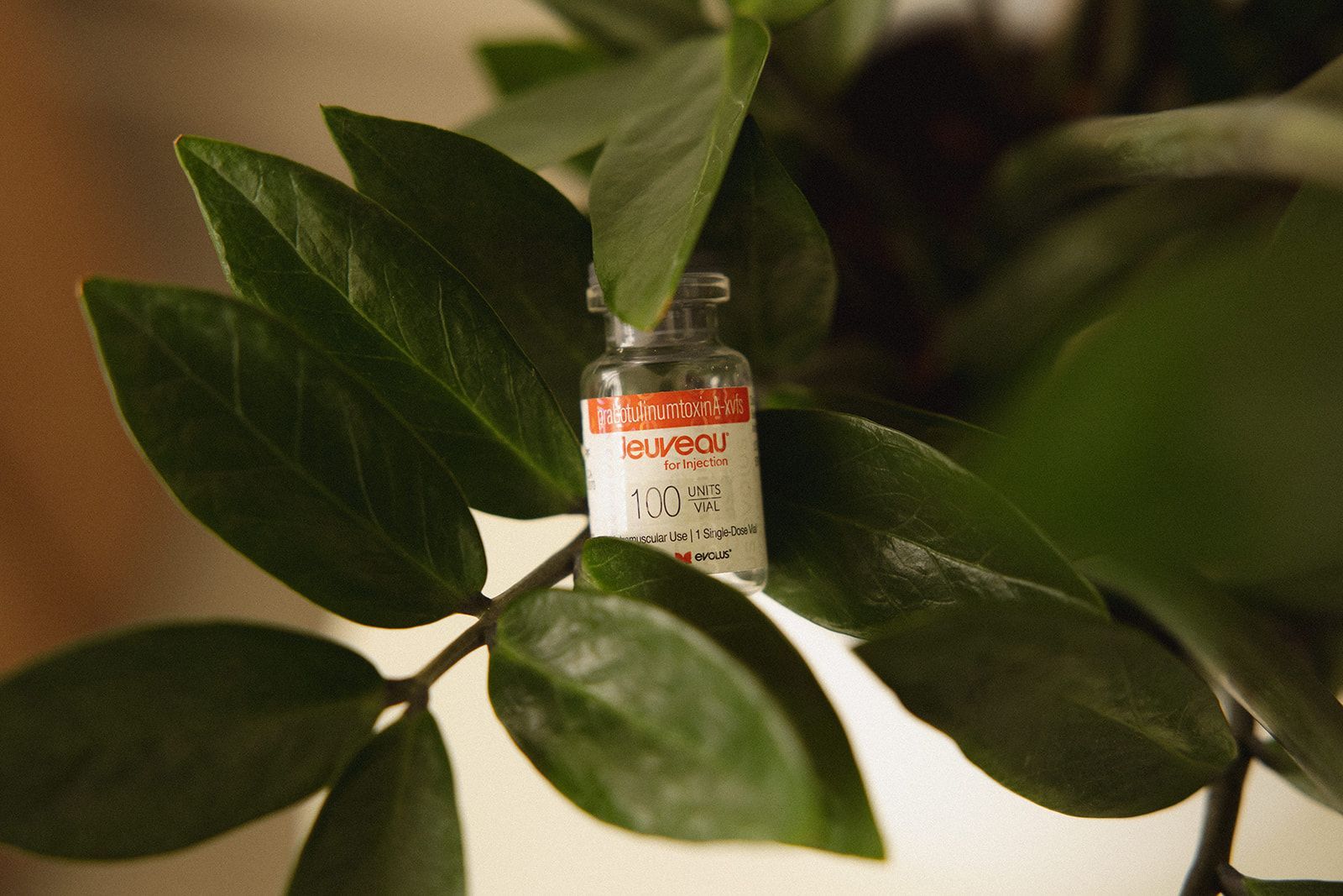 A small, clear glass vial with a red-and-white label sits nestled among the green leaves of a plant.