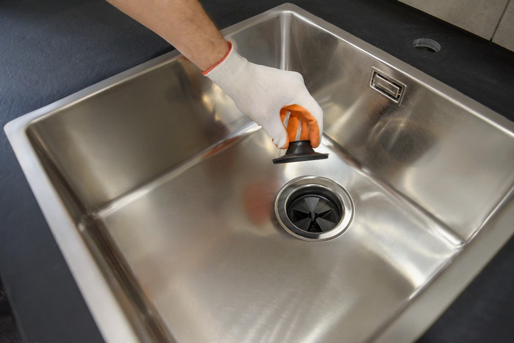 Gloved hand cleaning a stainless steel sink with an orange sponge