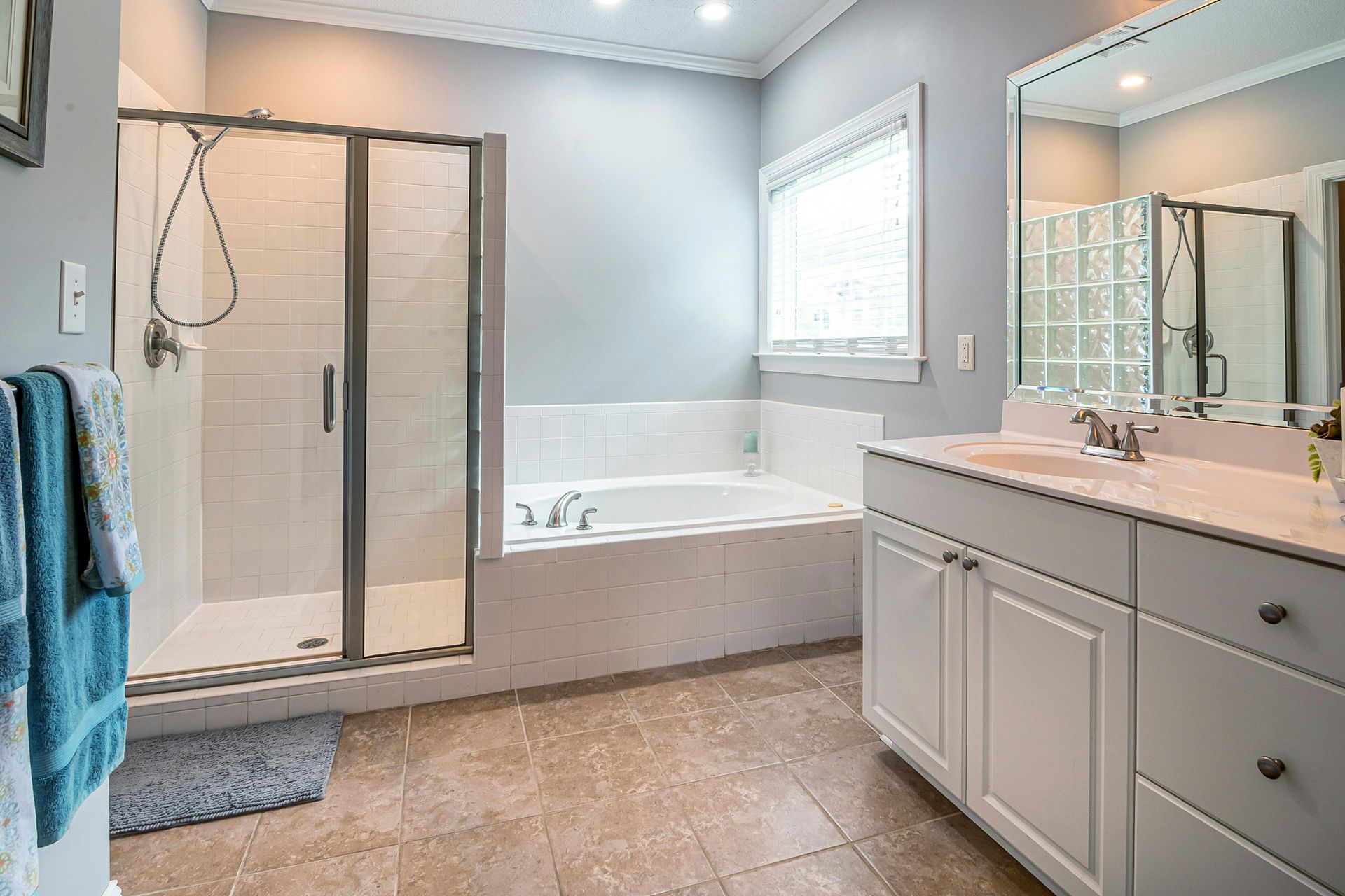 Modern bathroom with a glass shower, bathtub, large mirror, and gray vanity.