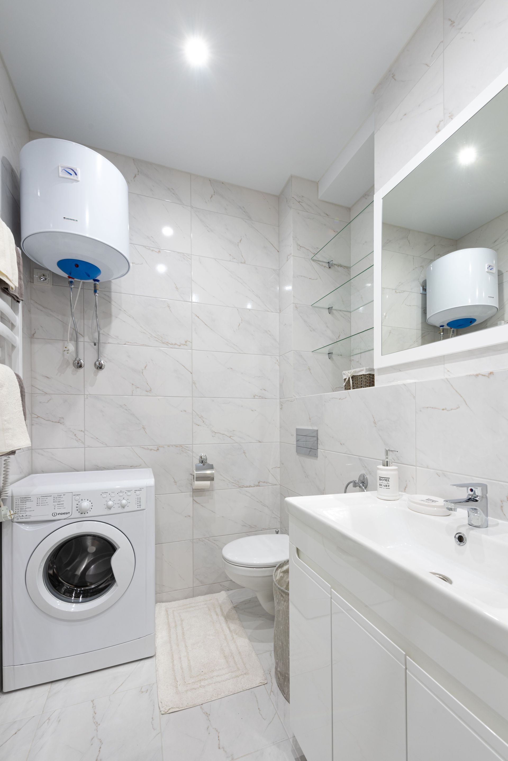 Bright white bathroom with washing machine, sink, toilet, mirror cabinet, and wall-mounted water heater