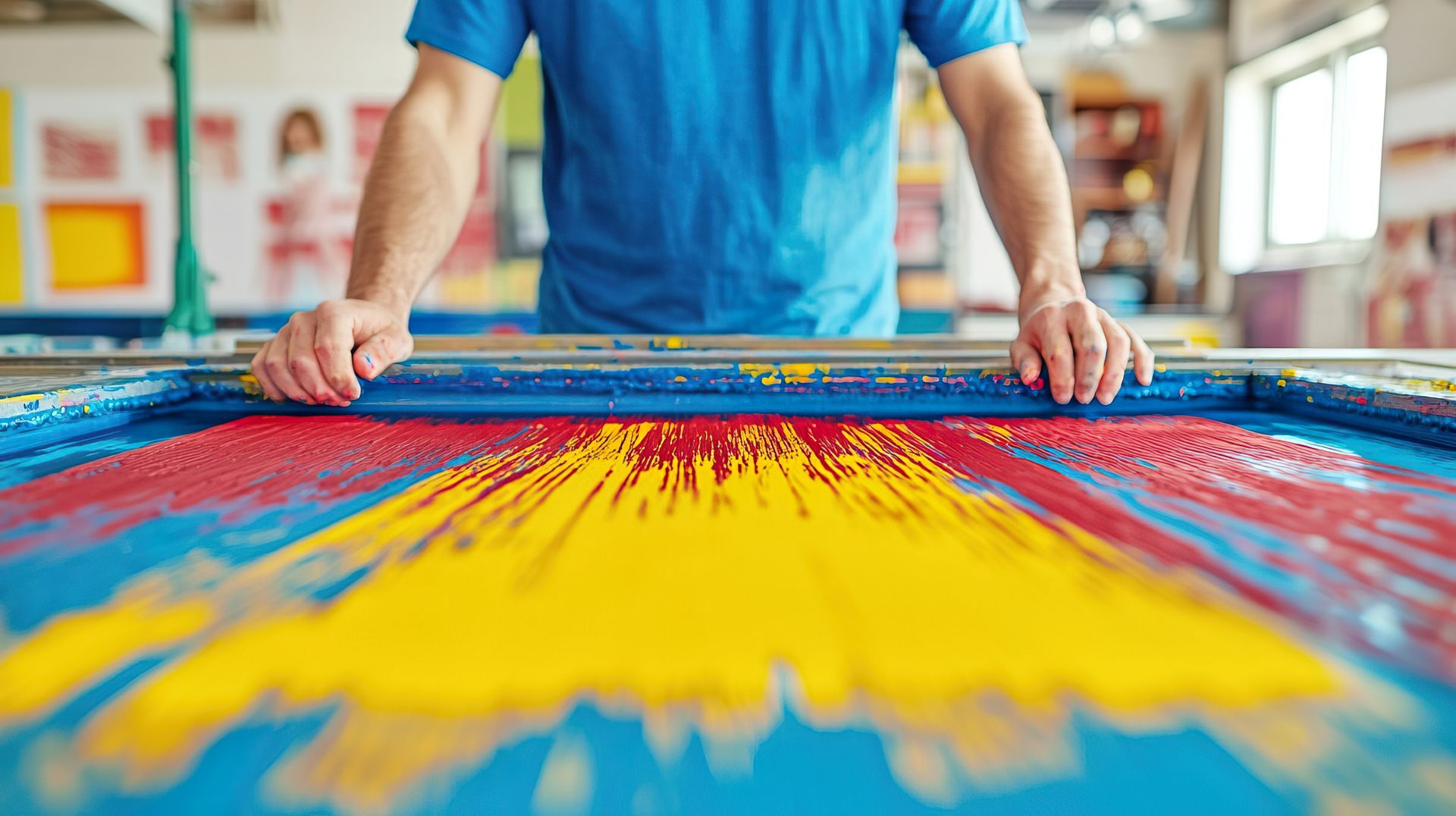 Person printing a vibrant multicolor design on a large fabric screen-printing table