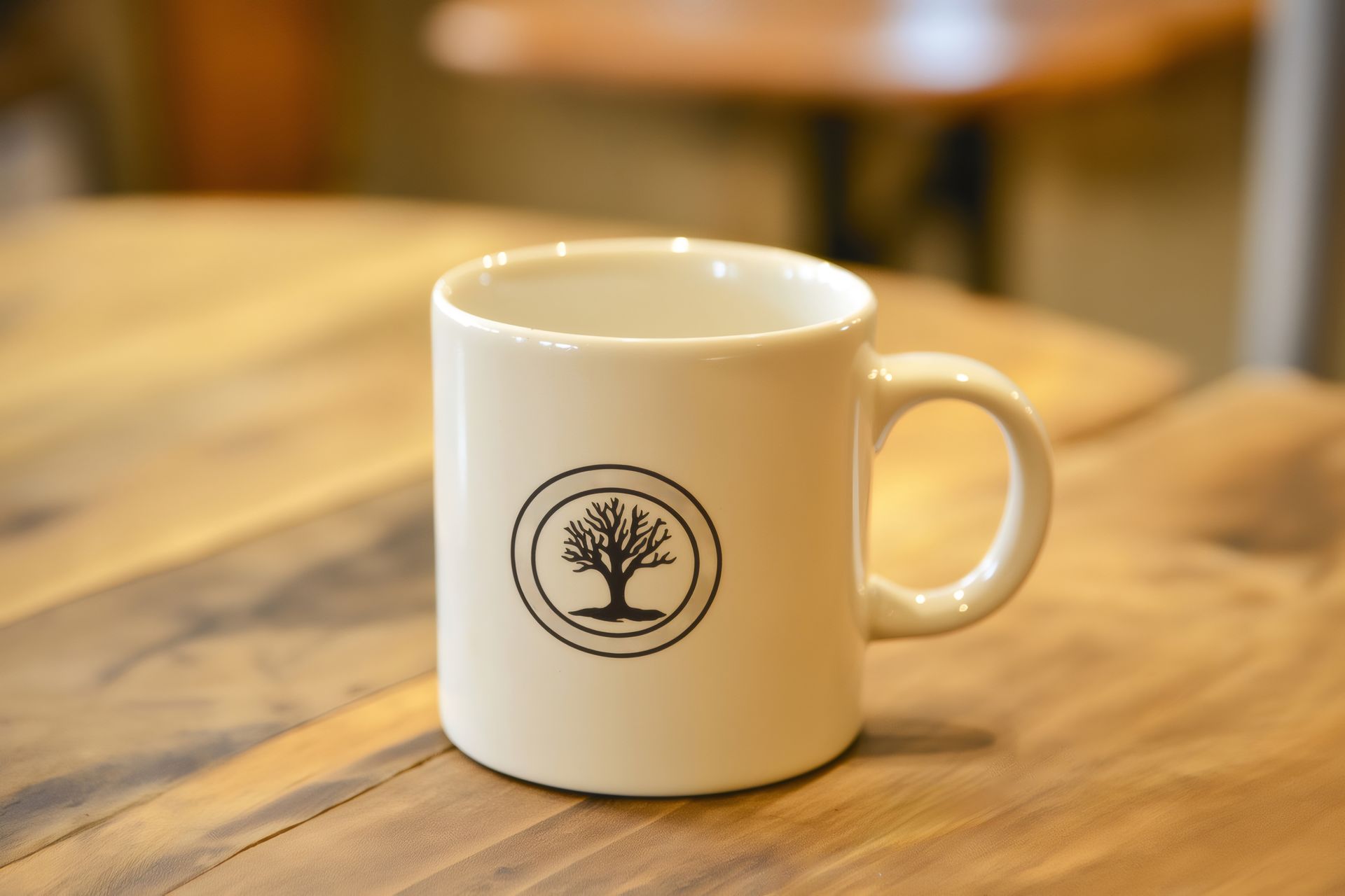White mug with a tree logo on a wooden table in a softly blurred café setting