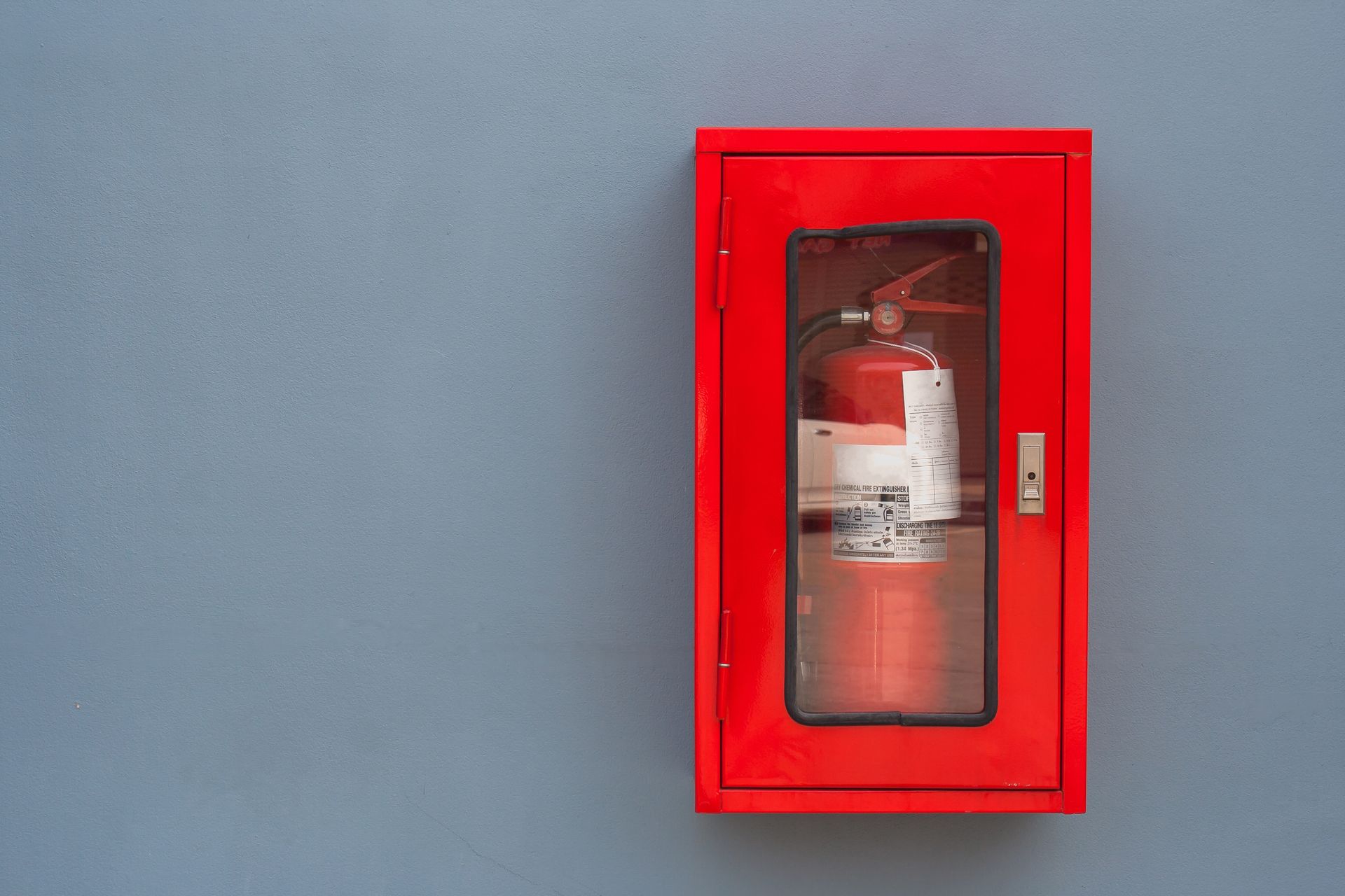 A fire extinguisher is inside a red cabinet, installed on a gray wall. A fire extinguisher is inside a red cabinet, installed on a gray wall.