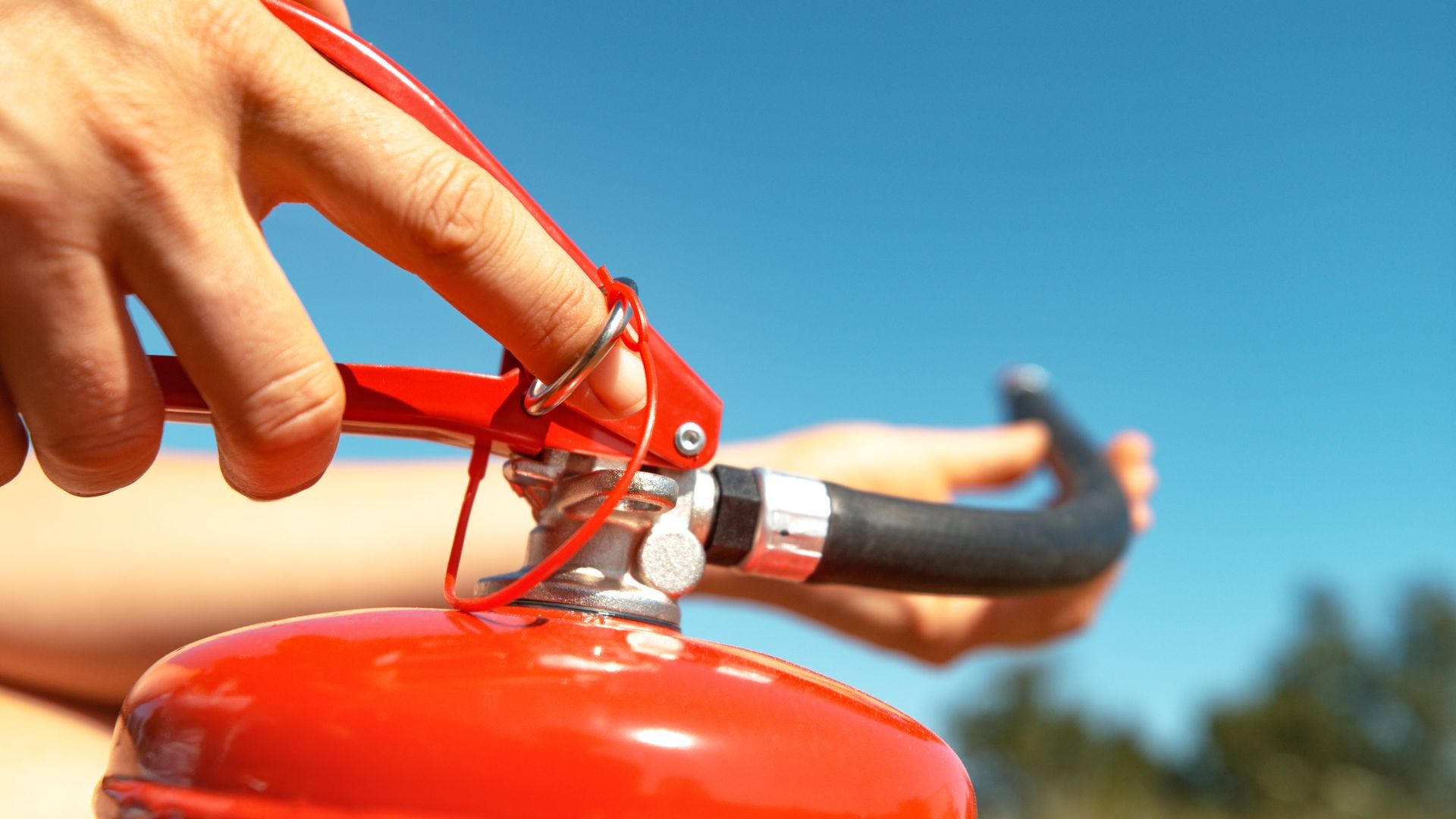A person presses the handle of a red fire extinguisher while aiming the hose outdoors. A person presses the handle of a red fire extinguisher while aiming the hose outdoors.