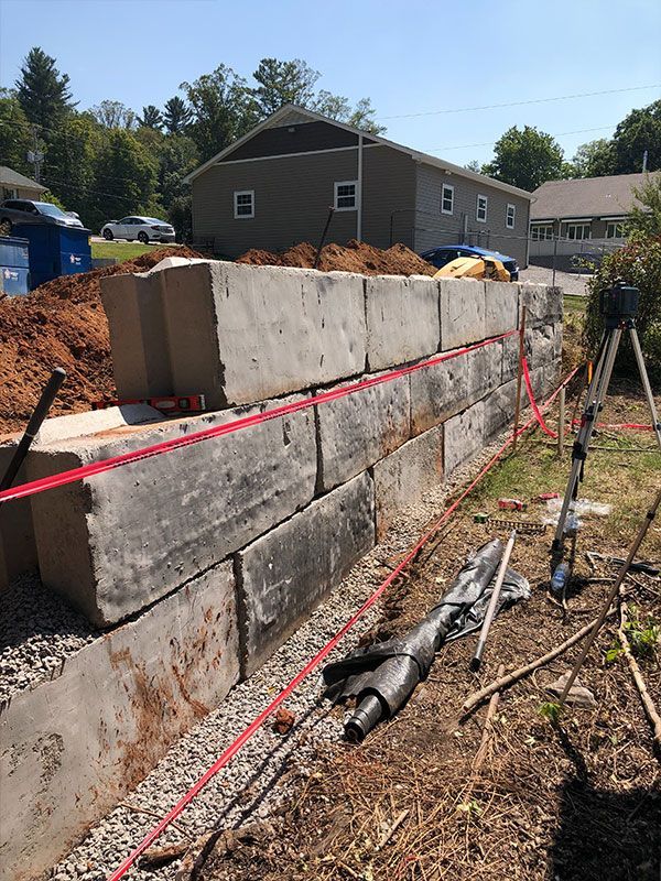 Partially built stone retaining wall with red string lines at a construction site in a wooded yard