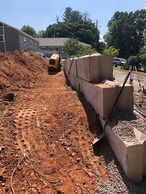 Construction site with excavator beside a dirt path and concrete retaining wall blocks