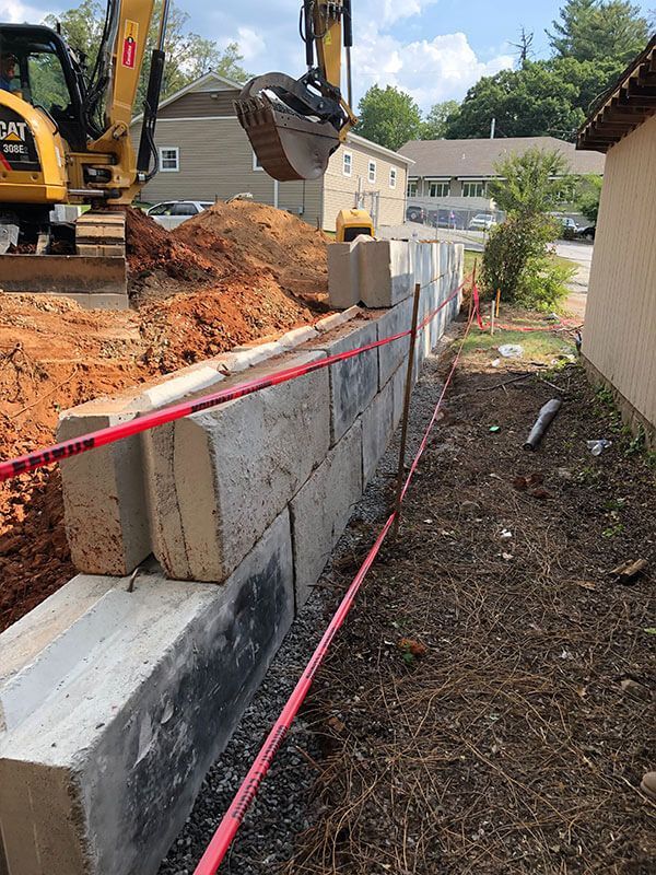 Construction site with excavator beside a red-taped retaining wall and dirt trench рядом