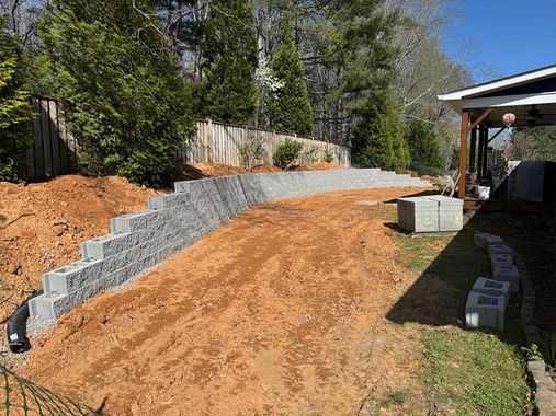 Freshly graded dirt slope beside a gray stone retaining wall and a house under construction