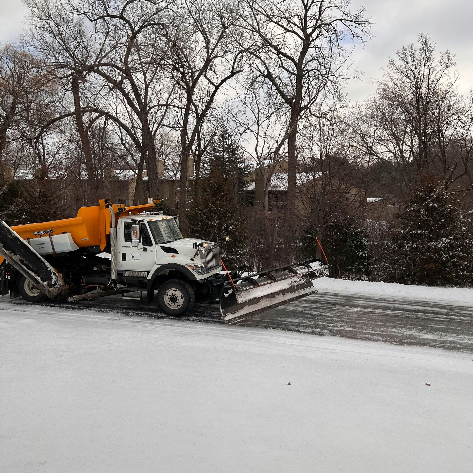 Black pickup plowing snow across a snowy field under a cloudy sky