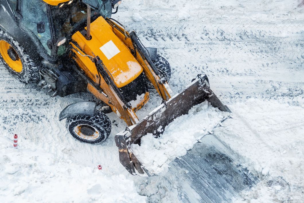 Orange snowplow clearing a snowy road, viewed from above.