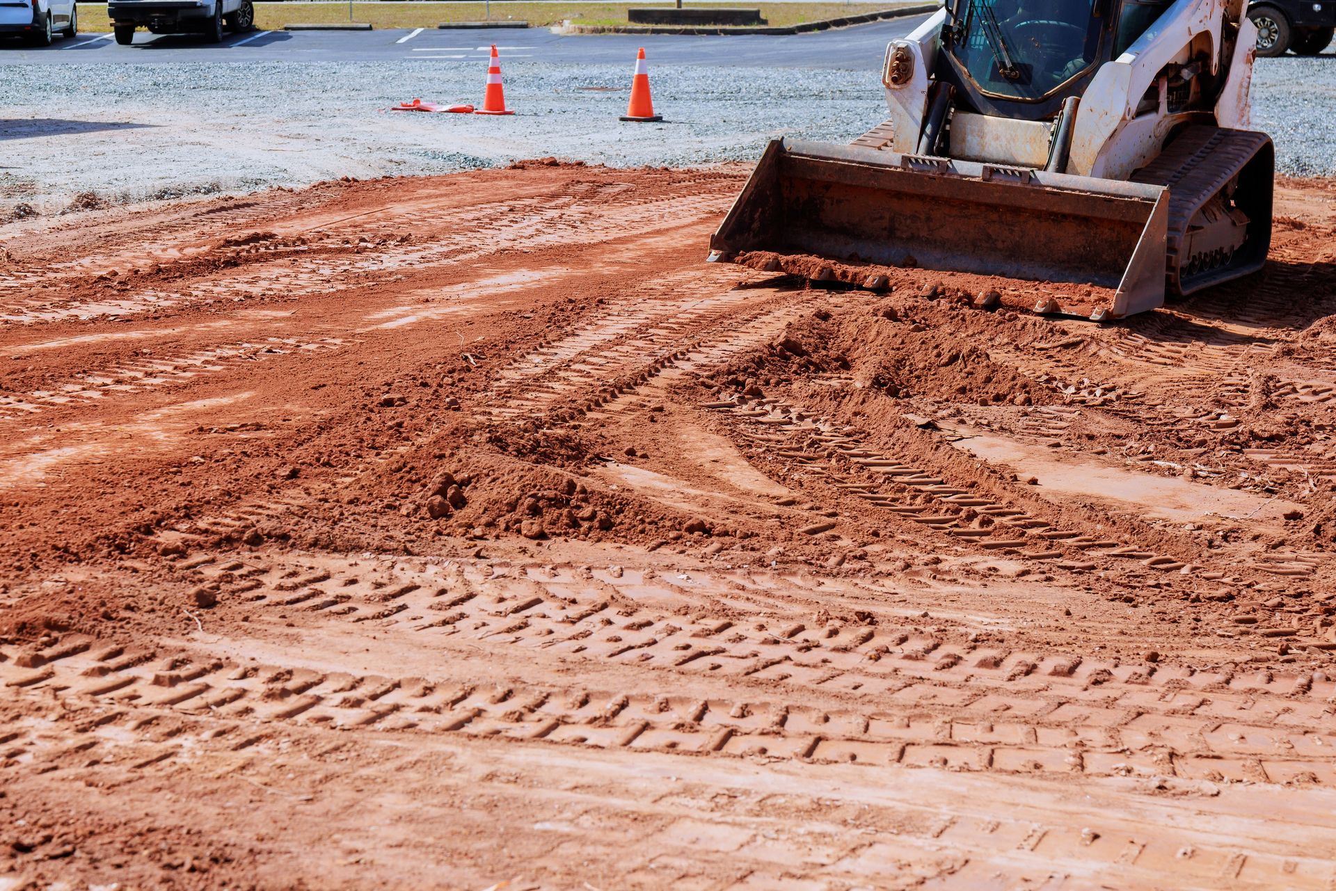 Construction loader grading muddy road with orange cones in the background