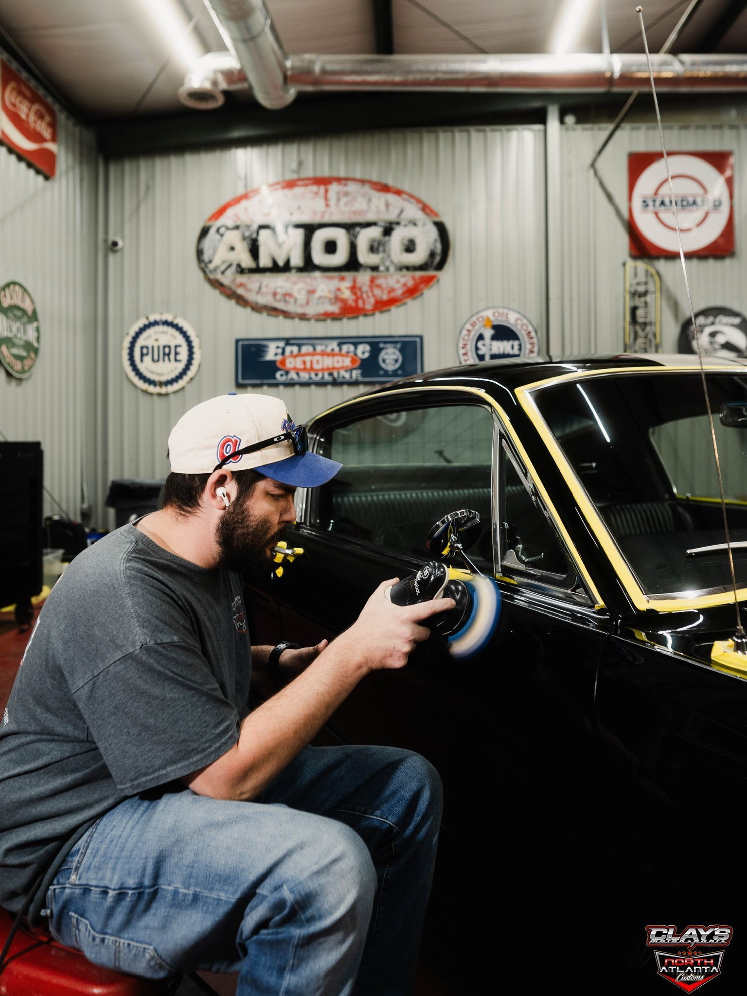 Man polishing a black vintage car in a garage with retro auto signs on the wall