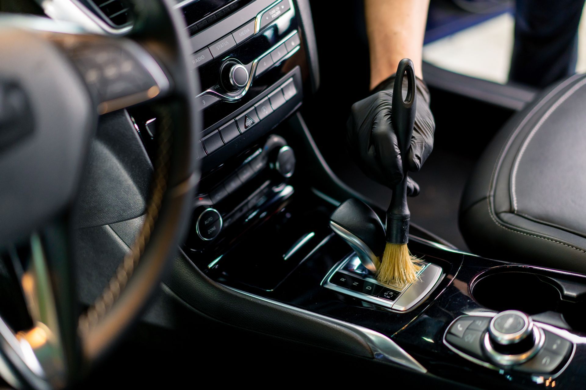 Gloved hand cleaning a car’s center console with a brush and spray bottle
